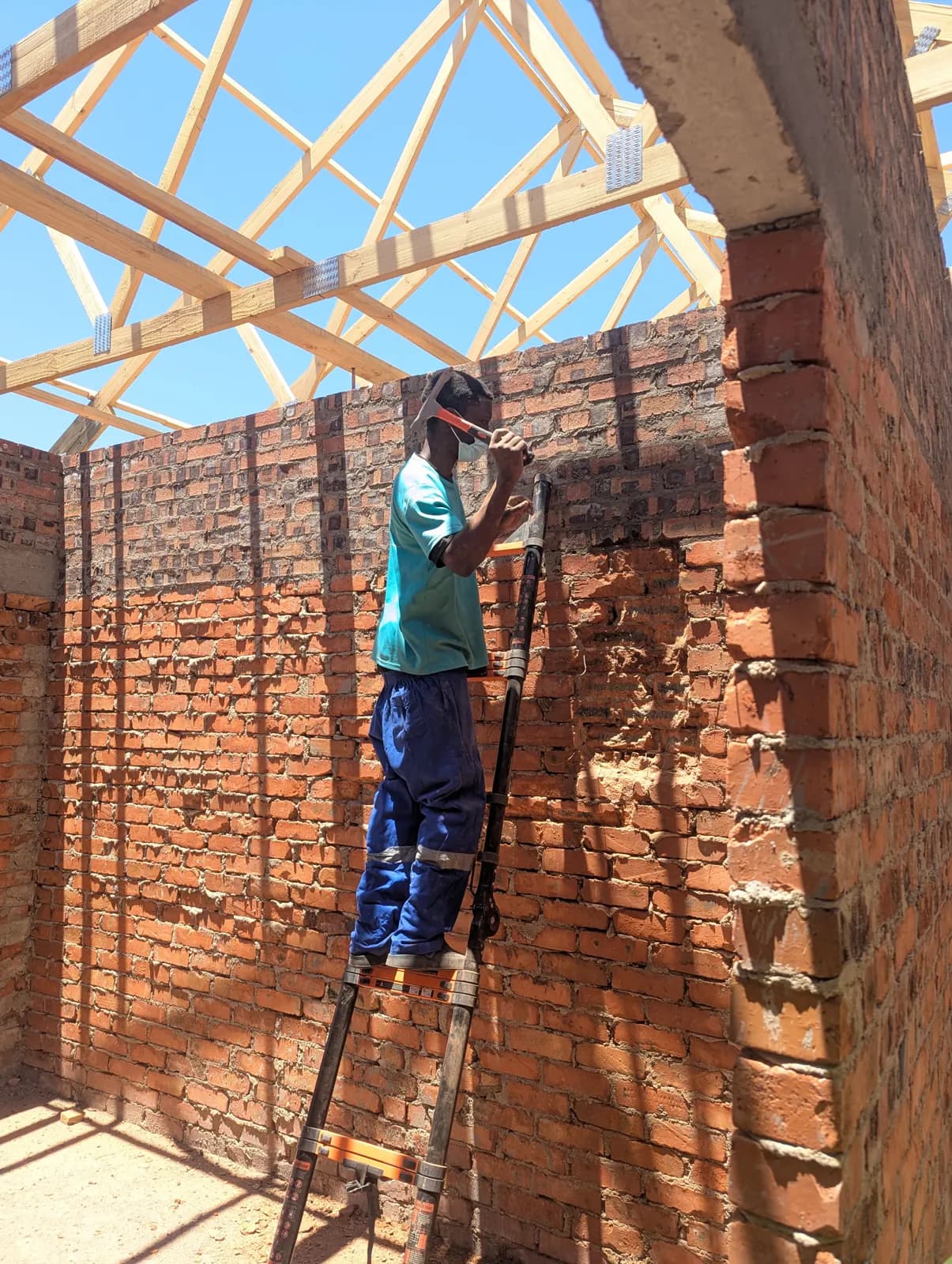 Tubing & Wiring: Cables run along the trusses before the roof is closed, with the ladder at the wall plate in Makonde, Zimbabwe