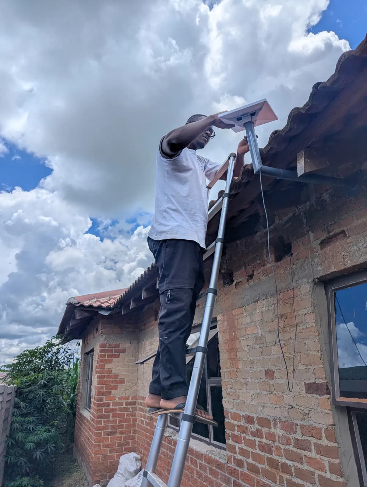 Techub technician on a ladder mounting a Starlink dish at the eaves of a brick house in Chinhoyi